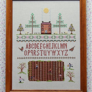 May include: A cross-stitch embroidery of a red house with a white door and windows, surrounded by trees, sheep, and a garden. The alphabet is stitched below the house, and the garden is filled with people working in the rows of plants.