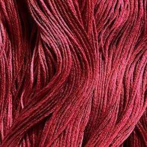 May include: Close-up of a bundle of deep red embroidery floss. The floss is arranged in a wavy pattern, showcasing the rich color and texture.