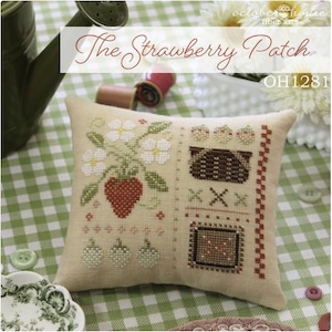 May include: A beige cross-stitch pillow with a strawberry patch design. The design includes a large red strawberry, white flowers, and a brown basket. The text "The Strawberry Patch" is at the top.
