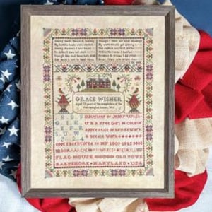 May include: Framed cross-stitch sampler with a gray wooden frame. The sampler features a detailed design with text and floral motifs in various colors. The text includes the name "GRACE WISMER" and other information. The sampler is displayed on a red, white, and blue background.