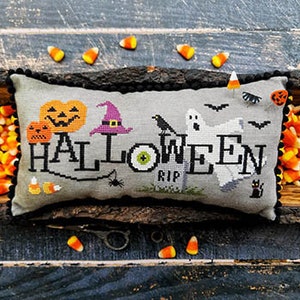 May include: A gray pillow with a cross-stitch design featuring the word "HALLOWEEN" in black thread. The design also includes pumpkins, a witch's hat, a ghost, a crow, a spider web, and a tombstone with the word "RIP".