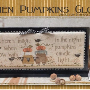 May include: Cross stitch pattern with a black frame and a white background. The pattern features two pumpkins with faces and the text "There's magic when glow with candle light".