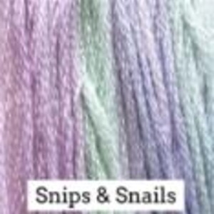 May include: A skein of yarn in a gradient of purple, green, and white colors. The yarn is labeled "Snips & Snails".