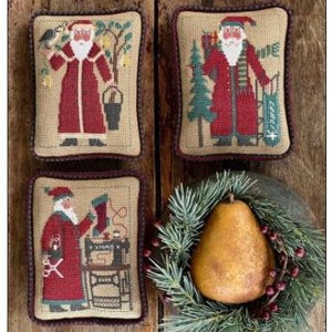 May include: Four decorative Christmas pillows with embroidered Santa Claus designs. Each pillow features a different Santa illustration in a red coat, with details like a bird, tree, and sewing machine. A pear and greenery complete the festive arrangement.