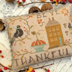 May include: A cross-stitch embroidery pattern featuring a house, a pumpkin, birds, and the text "Be Ye Thankful".