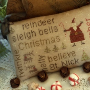 May include: A beige cross-stitch pillow with the words "reindeer", "sleigh bells", "Christmas", "believe", and "St. Nick" embroidered on it. A small Santa Claus figure is also embroidered on the pillow. The pillow is surrounded by brown jingle bells and candy canes.