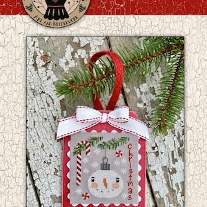 May include: A red and white Christmas ornament with a snowman design. The ornament has a white bow and a red ribbon for hanging. The text "Frosty Bulb" is at the top. The ornament is part of the Chantelle's 141 Ornament Box.