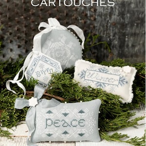 May include: A collection of embroidered winter-themed ornaments. The ornaments are in various shapes, including a round ball, a rectangle, and a small tag. The ornaments are light blue with white and dark blue cross-stitch designs and the words "Winter" and "Peace".