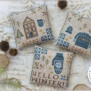 May include: Three decorative winter-themed pillows with cross-stitch designs. One pillow features a house and mug, another a sweater and hat, and the third a mitten with the text "HELLO WINTER!". The design is by Brenda Gervais.
