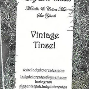 May include: A close-up of a bag of silver and white metallic tinsel. The bag is labeled "Lady Dot Creates" and "Vintage Tinsel". The label also includes the text "Metallic & Cotton Mix" and "Six Yards".