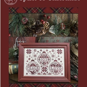 May include: Counted cross stitch pattern featuring three red and white Christmas ornaments with the words "Peace", "Joy", and "Love" embroidered on them. The pattern is framed in a red frame and surrounded by a plaid background.