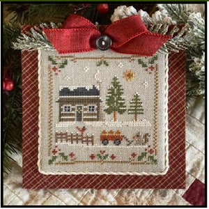 May include: A cross-stitch pattern of a winter scene with a small cabin, a tree, a red wagon, and a horse. The scene is framed in a red and white plaid fabric.