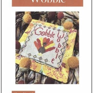 May include: Cross stitch pattern featuring a turkey with the text "Gobble Wobble" in a white frame with a yellow and brown background. The pattern is titled "Gobble Wobble" and is chart number 35.