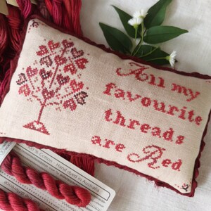 May include: A hand-stitched pillow with a red embroidered tree and the text "All my favourite threads are Red". The pillow is on a white surface with red embroidery floss and a tag that reads "100% Cotton - Hand dyed in Australia".