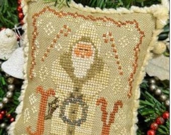 May include: A square, beige cross-stitch ornament with a Santa Claus design and the word "JOY" in orange. The ornament has a cream-colored fringe and a loop for hanging. Festive holiday decor.