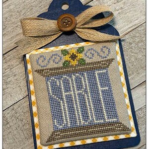 May include: A cross-stitch design on a blue background with a yellow and white checkered border. The design features a sunflower and the word "SALE" in blue letters.