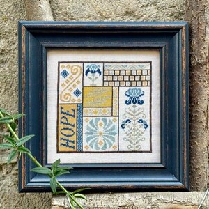 May include: Framed cross-stitch artwork with a navy blue wooden frame. The artwork features a patchwork design with floral and geometric patterns in yellow, blue, and cream colors. The word "HOPE" is vertically stitched on the left side.
