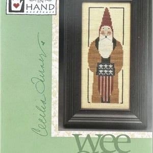 May include: Wee One Wee Santa 2002 cross stitch pattern by Heart in Hand needleart. The pattern features a small Santa Claus holding a flag with stars.