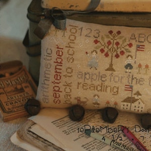 May include: A cross-stitched pillow with a school theme, featuring the words "apple for the teacher" and "back to school." The design includes a tree with red apples, children, and a schoolhouse. The pillow measures 7.5 inches by 4.5 inches.