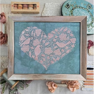May include: A framed cross-stitch artwork featuring a pink floral heart design with birds on a teal background. The artwork is in a wooden frame. The image also includes a box of darning and mending cotton.