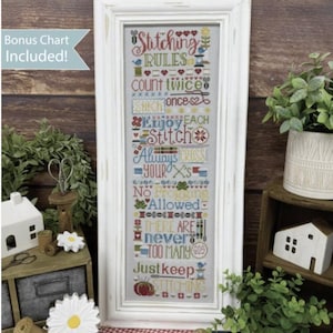 May include: A white framed cross stitch sampler with the text "Stitching Rules" and a list of rules for cross stitching. The sampler is surrounded by a red and white gingham pattern.