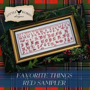 May include: A framed cross-stitch sampler with red lettering and illustrations, including the alphabet and numbers. The sampler is in a gold frame, surrounded by greenery and berries. The text "FAVORITE THINGS RED SAMPLER" is at the bottom.