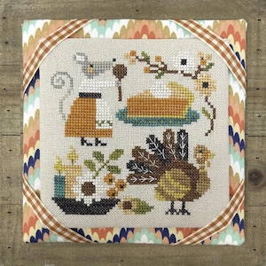 May include: Cross-stitch artwork featuring a Thanksgiving theme. The design includes a mouse, a slice of pie, a turkey, and floral elements. The artwork is framed with a patterned fabric and a brown and white ribbon.