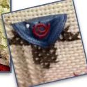 May include: Close-up of a cross-stitch design featuring a blue triangle with a red rose in the center. The design is on a cream-colored fabric with brown cross-stitch details. The image is framed with a white border.