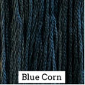 May include: Close-up of a bundle of dark blue cotton embroidery floss. The floss is tightly wound and has a smooth texture. The text "Blue Corn" is printed below the floss.