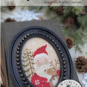 May include: A cross-stitch pattern titled MR. CLAUS by Brenda Gervais, featuring a Santa Claus and a reindeer next to a Christmas tree. The design is displayed in an oval black frame with beaded detailing and includes the text #CS387 Pixie Pics.