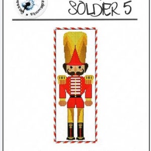 May include: A red and gold Nutcracker soldier cross stitch pattern with a candy cane border. The pattern is titled "Nutcracker Soldier 5".