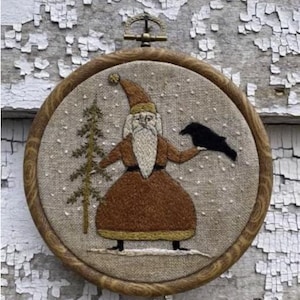 May include: Embroidered hoop art featuring a Santa Claus figure in a red and gold robe, holding a black bird. The background is a beige linen fabric with a snowy design.