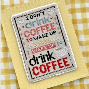May include: Cross-stitch artwork in a yellow frame. The artwork features the text "I DON'T drink COFFEE TO WAKE UP I WAKE UP TO drink COFFEE" in black, red, and blue. Coffee cup motifs are also included.