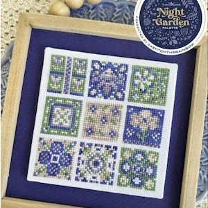 May include: A framed cross-stitch sampler with a blue background. The sampler features nine square panels with floral and geometric patterns in shades of blue, green, and beige. A circular sticker with the text "Night Garden Palette" is in the upper right corner.