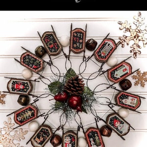 May include: A collection of 12 cross-stitch patterns for sled ornaments. The patterns are arranged in a circle around a pine cone and holly berries. The patterns feature various winter themes, including snowmen, reindeer, and Christmas trees. The text "Lets Go Sledding! 12 Sled Ornament Designs!" is at the top of the image. The text "102" is at the bottom of the image. The text "Annie Beez" is in a circle at the bottom right of the image.
