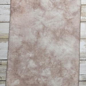 May include: A piece of fabric with a mottled, tie-dye effect in shades of brown and white. The fabric has a textured appearance and a visible weave. The top edge is finished with a line of orange stitching.