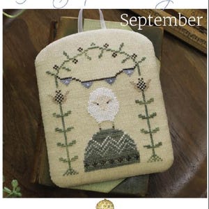 May include: A cross-stitch pattern featuring a white sheep standing on a green hill with a blue and brown bunting hanging above. The pattern is titled "The Shepherd's Year September" and is from October House Fiber Arts.