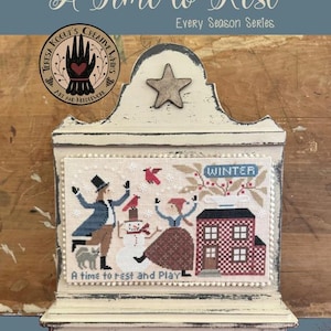 May include: A decorative wooden shelf with a star and a cross-stitch winter scene. The cross-stitch features a couple, a snowman, a cat, and a house. The text reads "A Time to Rest" and "A time to rest and Play".