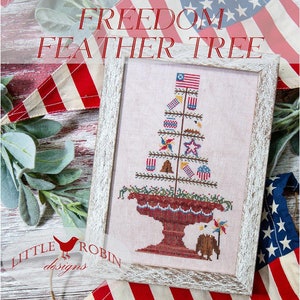 May include: A cross-stitch pattern of a "Freedom Feather Tree" with red, white, and blue patriotic decorations. The design is framed in a white wood frame and features a turkey holding a pinwheel. The text "Little Robin Designs" is visible in the bottom left corner.