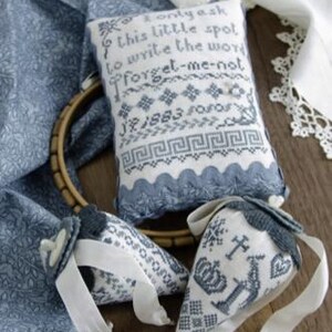 May include: Three blue and white embroidered fabric pieces. The largest piece is a pillow with the text "I only ask this little spot to write the word forget-me-not" and the date "J.F. 1883". The other two pieces are smaller and have a more intricate design.