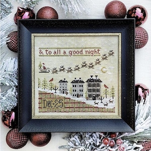 May include: A cross-stitch pattern featuring a winter scene with houses, a sleigh pulled by reindeer, and the text '& to all a good night'. The pattern is framed in a black frame with a gold trim. The date 'Dec 25' is stitched in the bottom right corner.