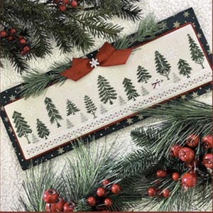 May include: A rectangular Christmas-themed cross-stitch design featuring a row of stylized green trees and snowflakes on a cream background. A red bow with a snowflake embellishment adorns the top. The design is framed by a dark blue border with white stars and red berries.