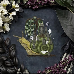 May include: Cross-stitch art of a snail with a green shell, carrying a spooky graveyard scene. The snail is yellow and green, with a weeping willow tree and white ghost figures. The background is dark blue.