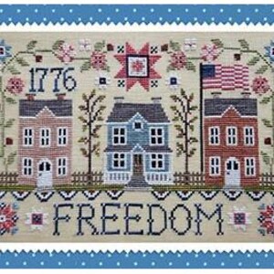 May include: A cross-stitch embroidery on beige fabric featuring three houses, the year 1776, an American flag, floral motifs, and the word FREEDOM in black lettering. The design is framed by a blue border with white polka dots and a scalloped edge.