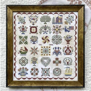 May include: Framed cross-stitch sampler with a gold-colored frame. The sampler features a grid of colorful, geometric and floral designs, including hearts, trees, and flowers. The text "T.R. 1842" is stitched in the center.