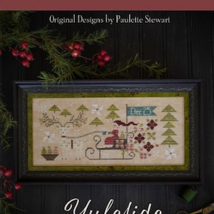 May include: A framed cross-stitch sampler with a winter scene of a sleigh pulled by a reindeer with the text "Yuleside Delivery" below the frame. The sampler is on a dark wood surface with a sprig of greenery and red berries.