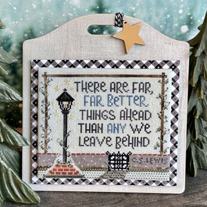 May include: A cross-stitch embroidery on a wooden plaque with a black and white checkered border. The embroidery features a street lamp with a quote: "There are far, far better things ahead than any we leave behind."
