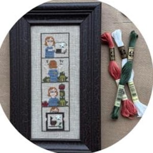 May include: A framed cross-stitch sampler with four panels depicting a person and various objects. The frame is dark brown. Beside the frame are three bundles of embroidery floss in red, white, and green.