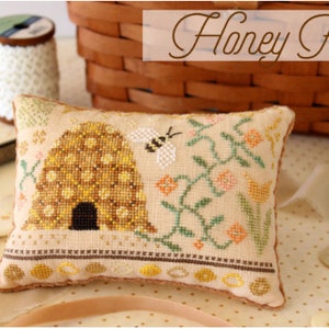 May include: A rectangular, embroidered pillow with a beehive and bee design. The pillow features a tan background with a detailed cross-stitch pattern in shades of yellow, brown, and green. The text "Honey Faire" and "OH1257" are visible.