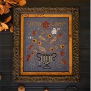 May include: A framed cross-stitch sampler titled October featuring a dark blue fabric background. The design displays a black urn filled with orange and gold floral elements, a small white ghost holding a flag, and a tiny bat, all enclosed in a dark ornate wooden frame.